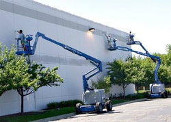 two large raised scaffolding holding two of our employees painting the exterior of a building in a grayish white color