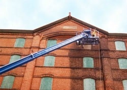 A large extended scaffolding raised up on the exterior of a brick building being painted