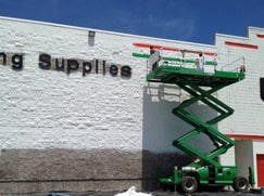 workers painting exterior of supply company on lift