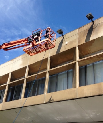 workers on a lift power washing exterior of building