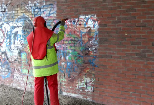 worker performing graffiti removal from a brick wall