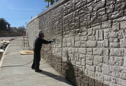 worker spray painting a stone wall