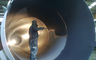 an industrial painter applying a coat of gray paint inside of a concrete tube structure