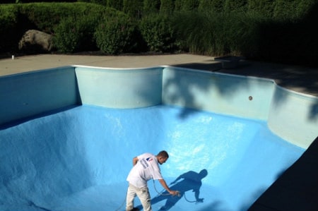 a member of our crew applying a perfect waterproof coating in bright blue at the bottom of a municipal pool