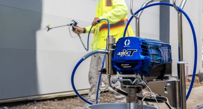 A worker spraying the side of a building with crisp, white, top of the line paint