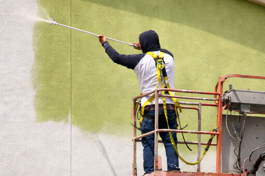 commercial painter spraying the side of a building with white paint